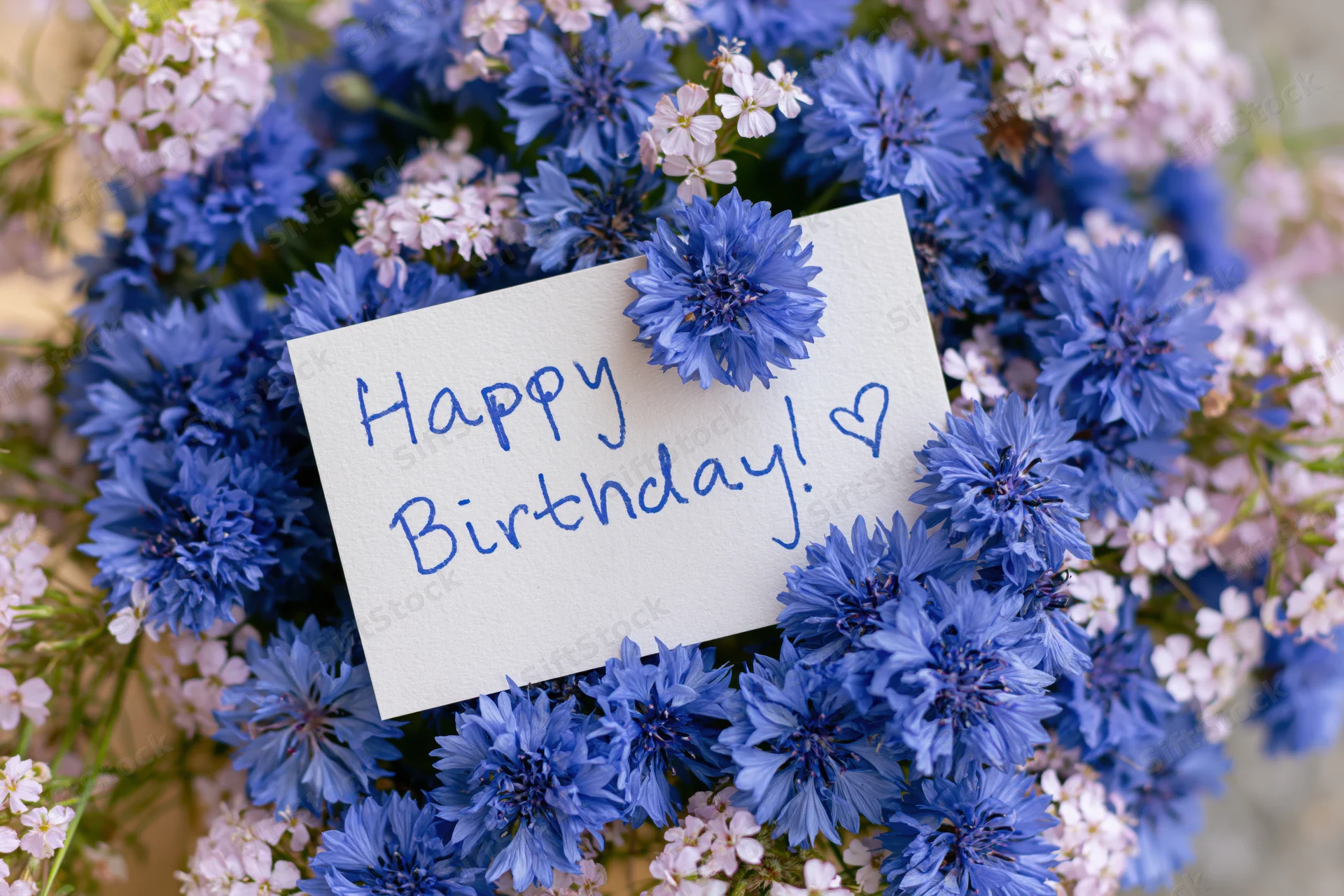 Blue and white flowers arranged around a handwritten birthday card with a heart symbol