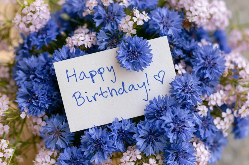 Blue and white flowers arranged around a handwritten birthday card with a heart symbol