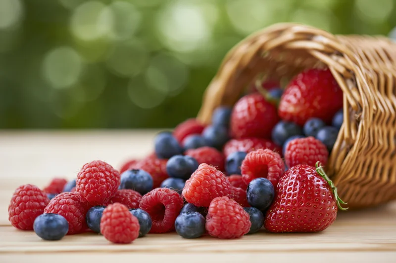 Spilled berries from a wicker basket on a wooden surface outdoors