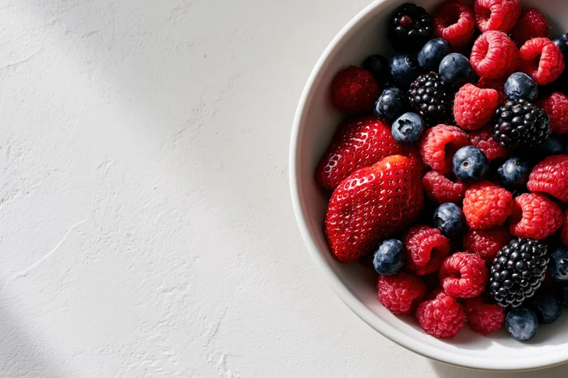 Mixed berries in a white ceramic bowl on a textured white surface