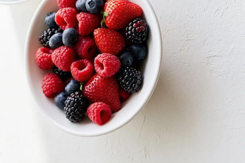 Mixed berries in a white ceramic bowl on a light surface