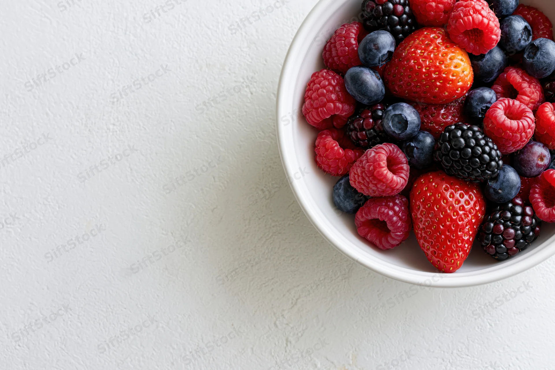 Mixed berries in a white ceramic bowl on a light surface