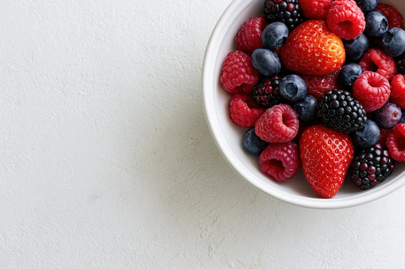 Mixed berries in a white ceramic bowl on a light surface