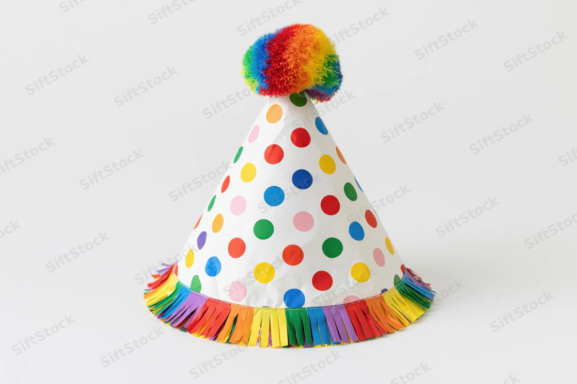 White conical party hat with rainbow pompon and colorful fringe on plain background