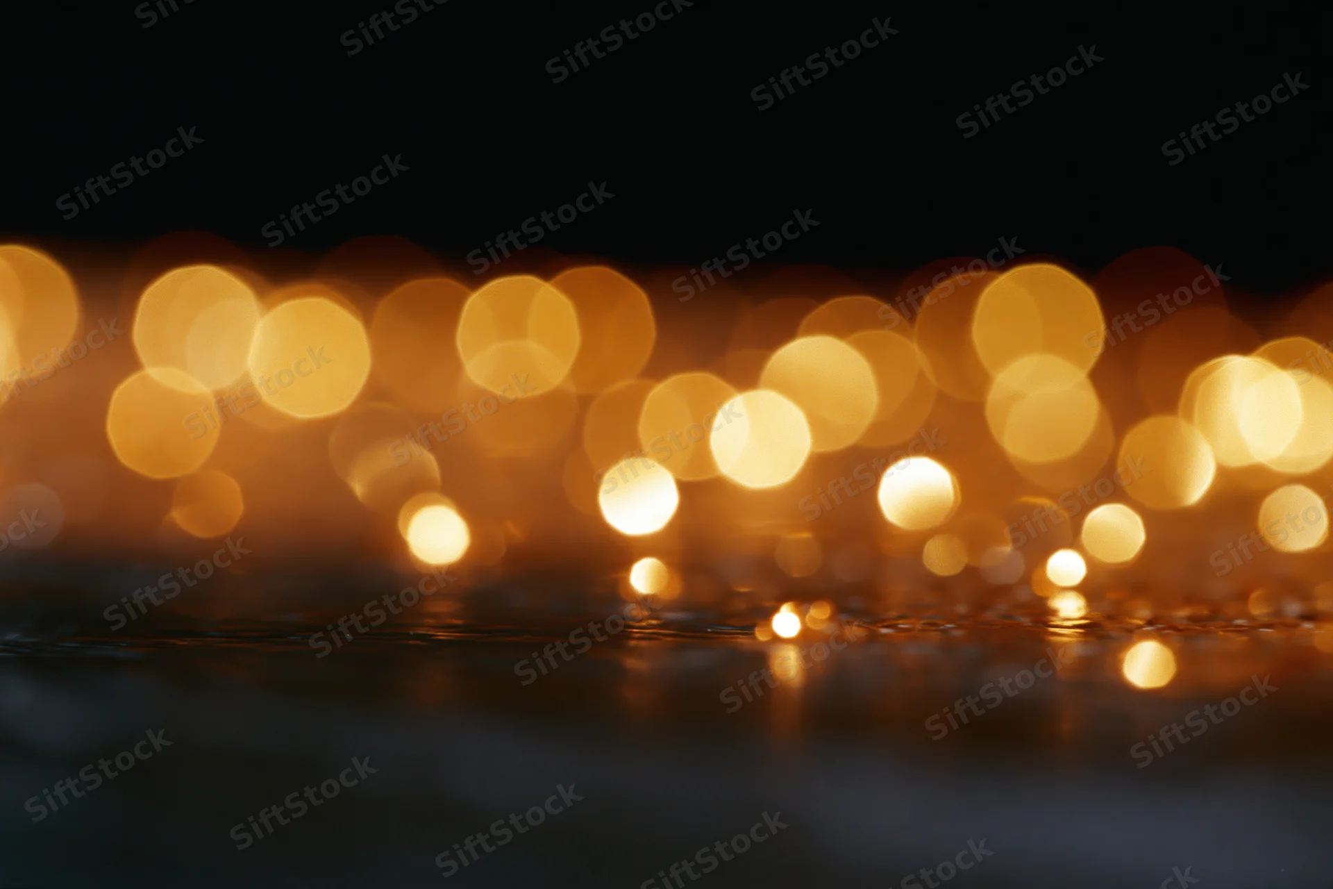 Golden bokeh lights reflecting on dark water at night