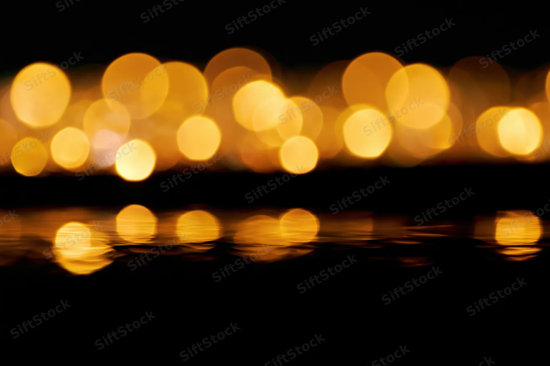 Golden bokeh lights reflecting on dark water at night