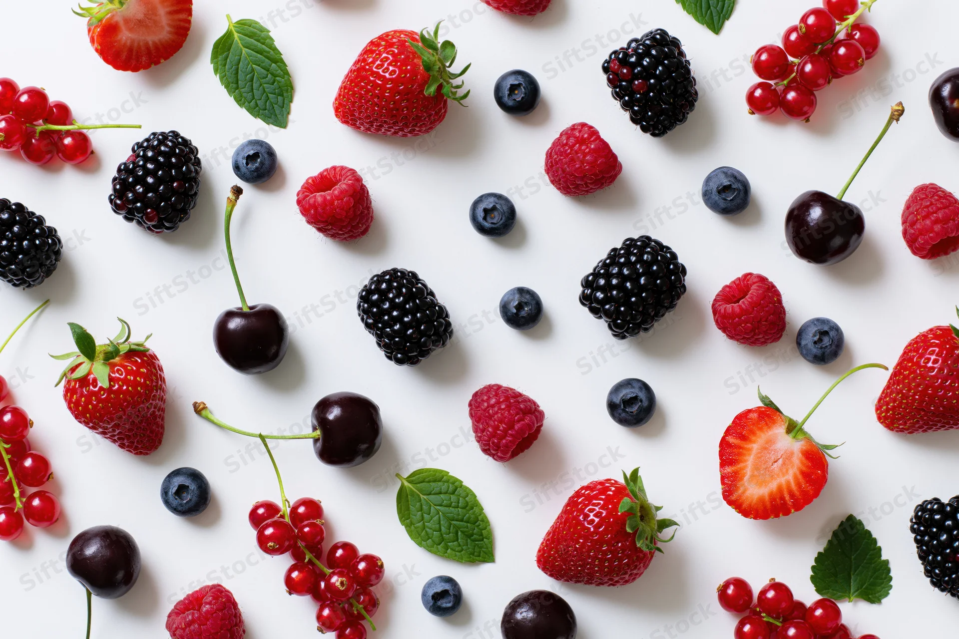 Assorted fresh berries and cherries scattered on white surface with mint leaves