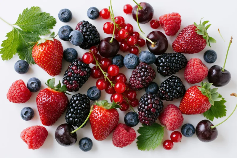 Assorted fresh berries and cherries scattered on a white surface
