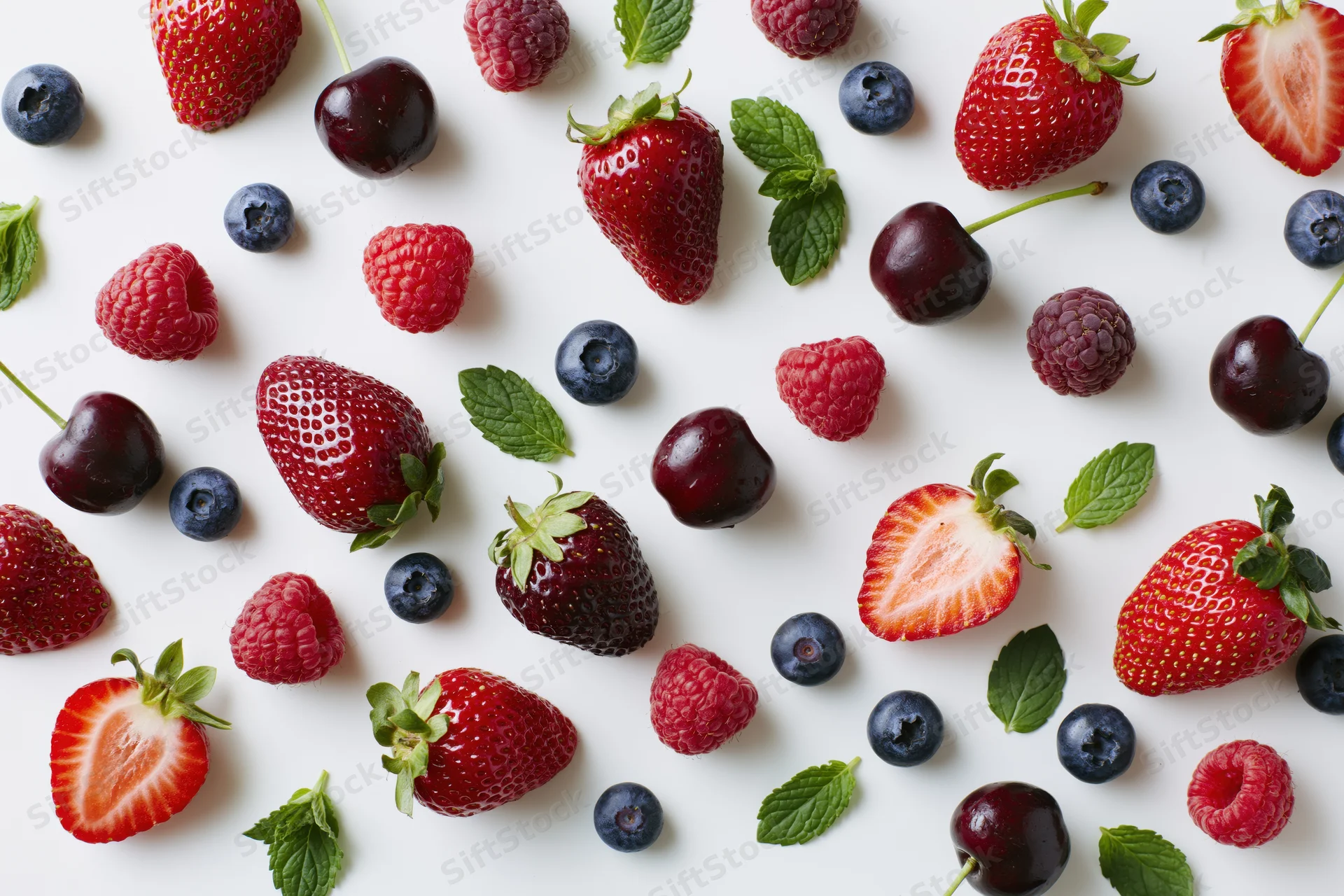 Fresh strawberries blueberries raspberries cherries and mint leaves scattered on white surface
