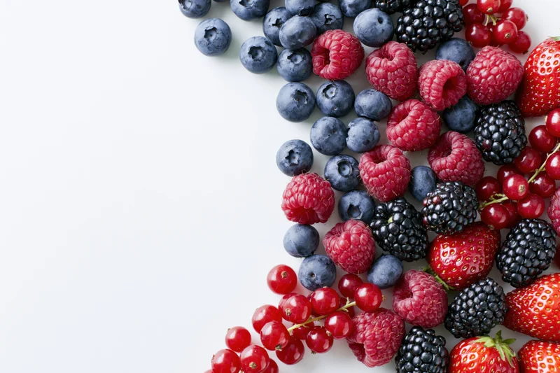 Assorted fresh berries arranged along the right edge on a white surface