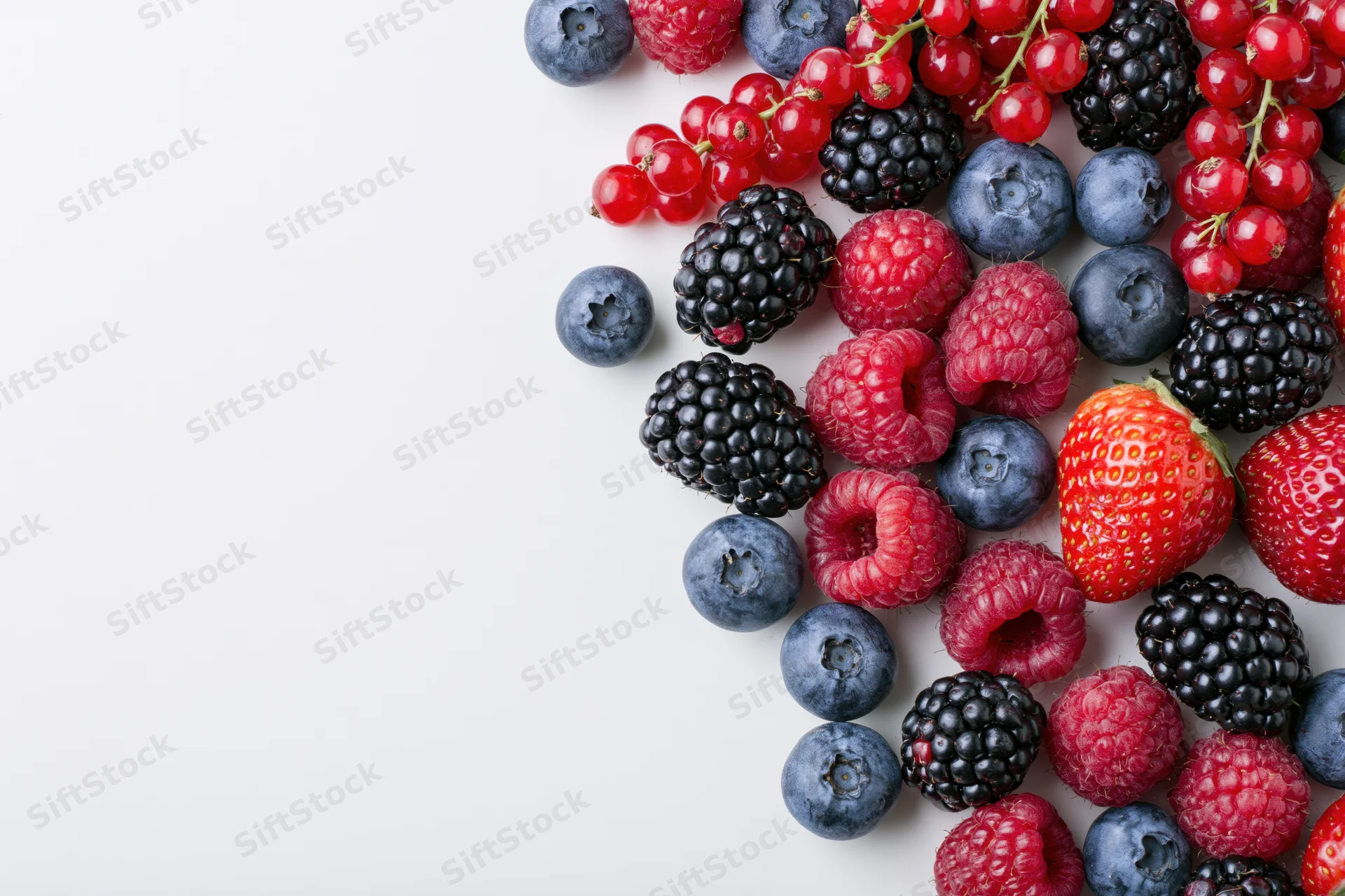 Assorted fresh berries arranged on white surface with copyspace