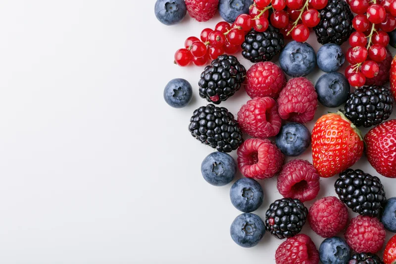Assorted fresh berries arranged on white surface with copyspace
