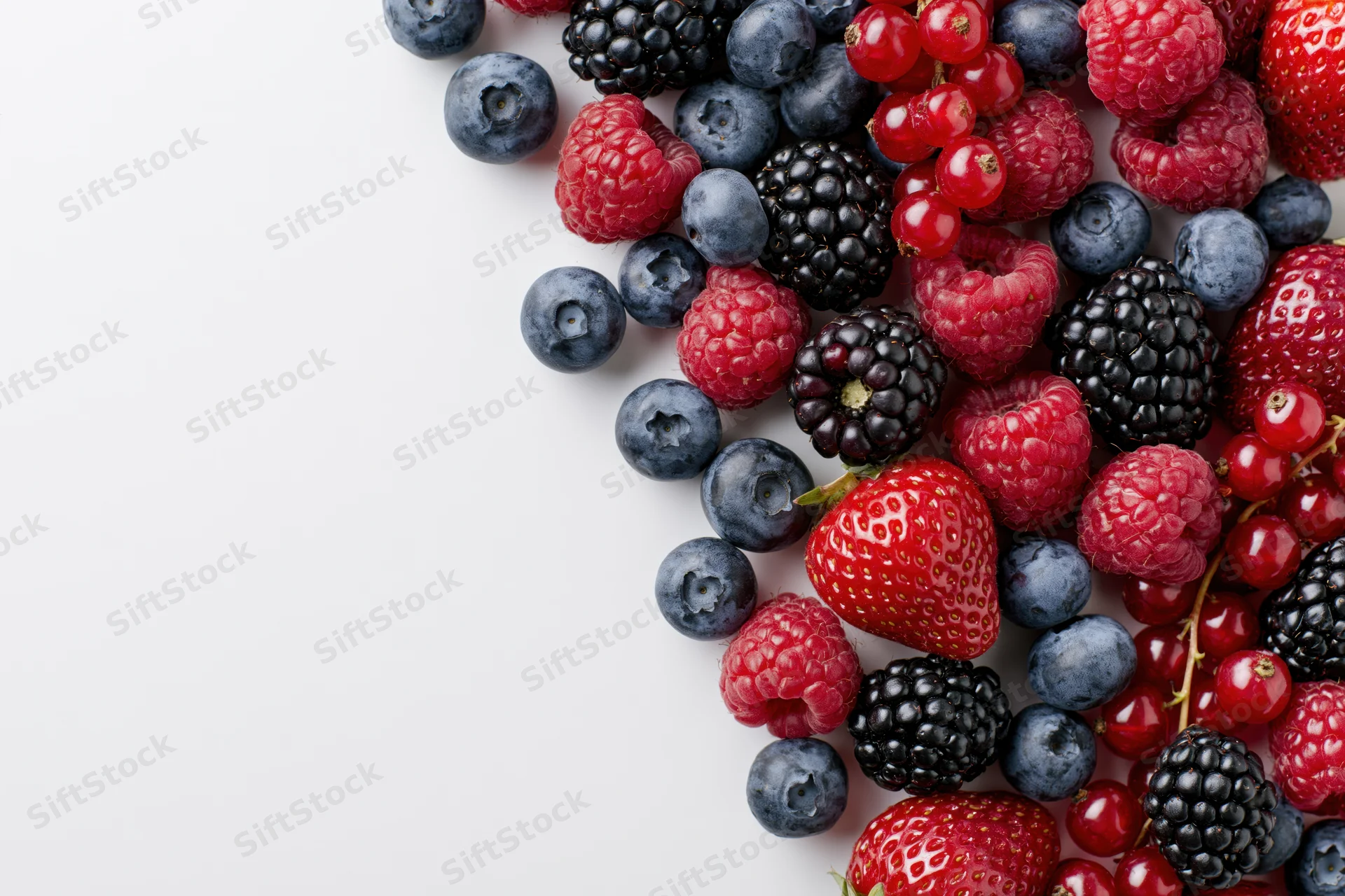 Assorted fresh berries arranged on white surface with copyspace