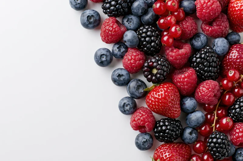Assorted fresh berries arranged on white surface with copyspace