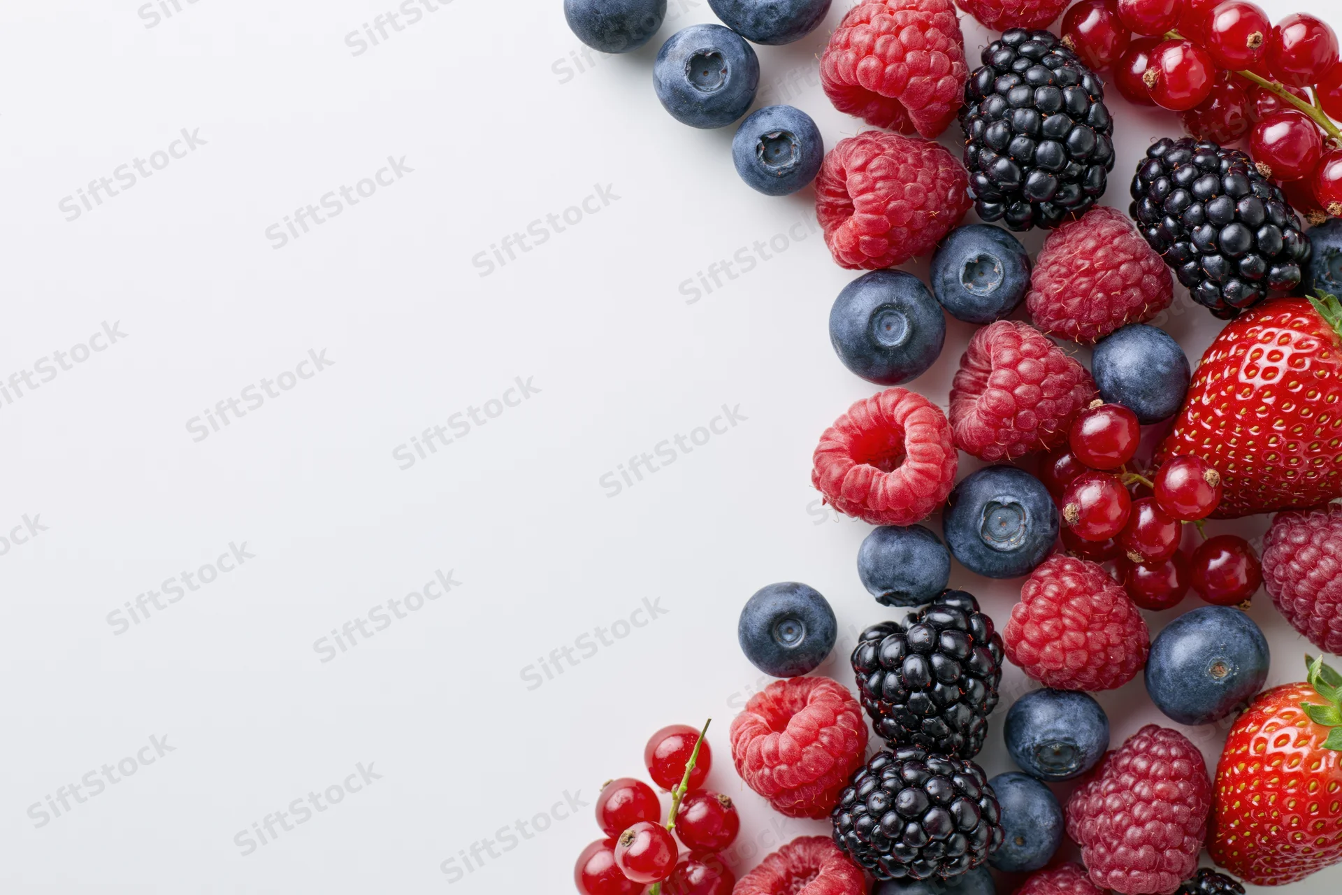 Assorted fresh berries arranged in a diagonal line on a white surface with copyspace