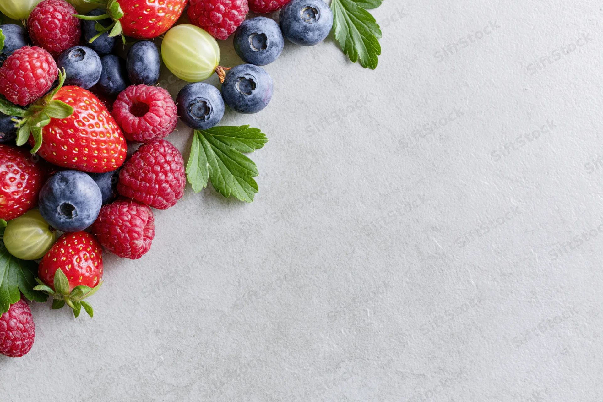 Assorted fresh berries arranged in upper-left corner on light surface with copyspace