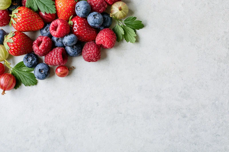 Assorted fresh berries arranged in upper left corner on light surface with copyspace