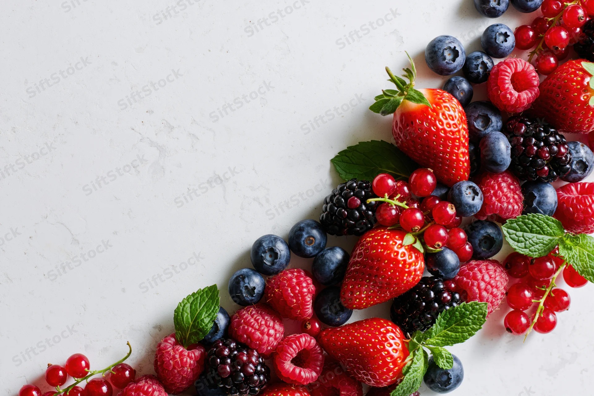 Assorted fresh berries arranged along the right edge of a white marble surface with copyspace on the left