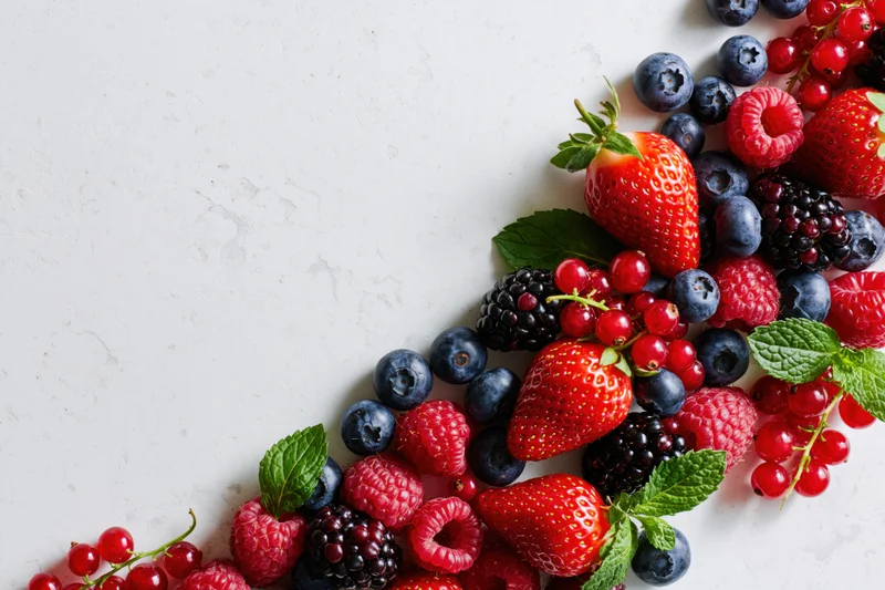 Assorted fresh berries arranged along the right edge of a white marble surface with copyspace on the left