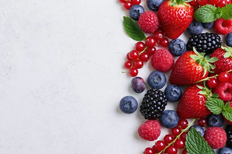 Assorted fresh berries arranged along the right edge of a white marble surface with copyspace on the left
