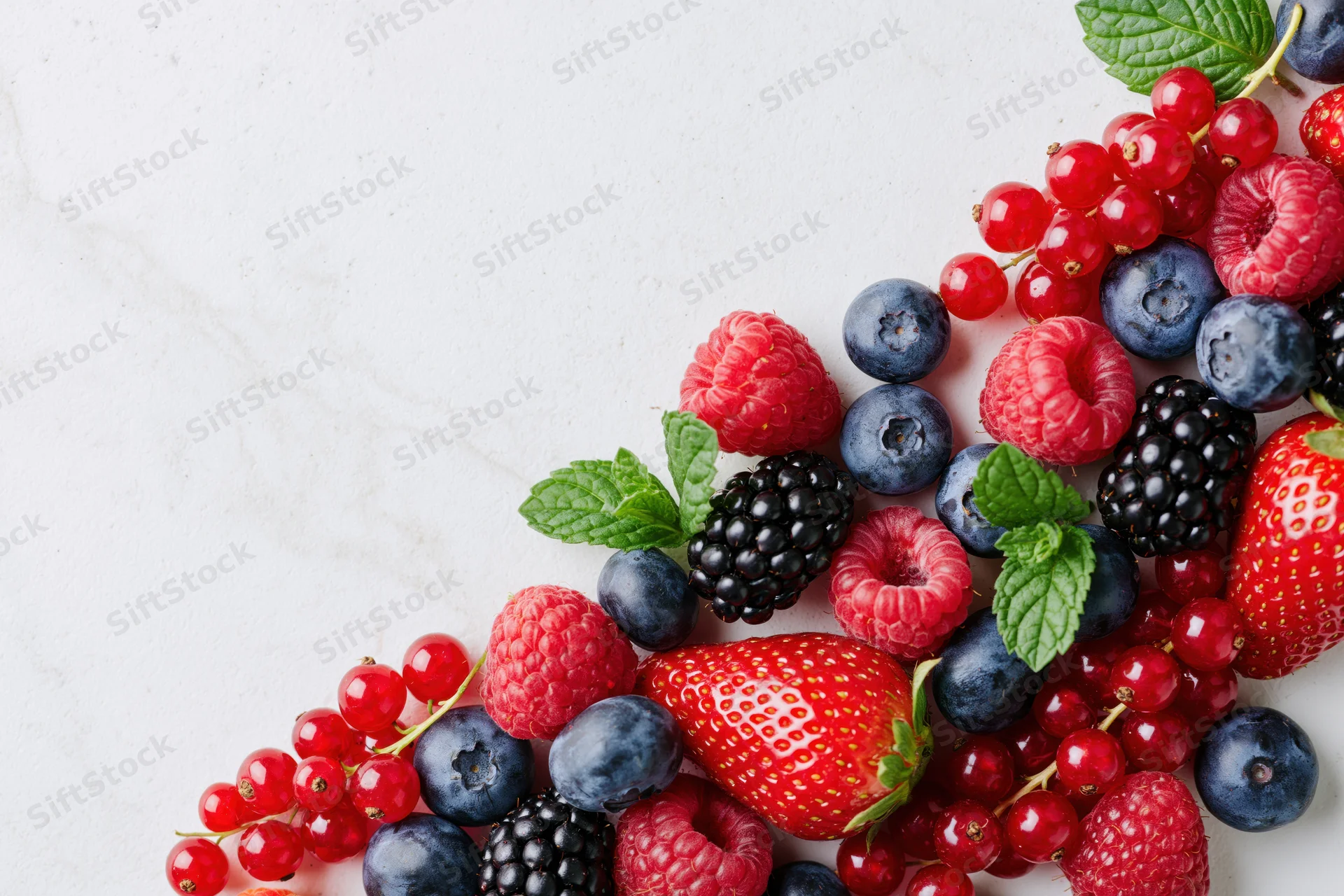 Assorted fresh berries and mint arranged along the right edge of a white marble surface