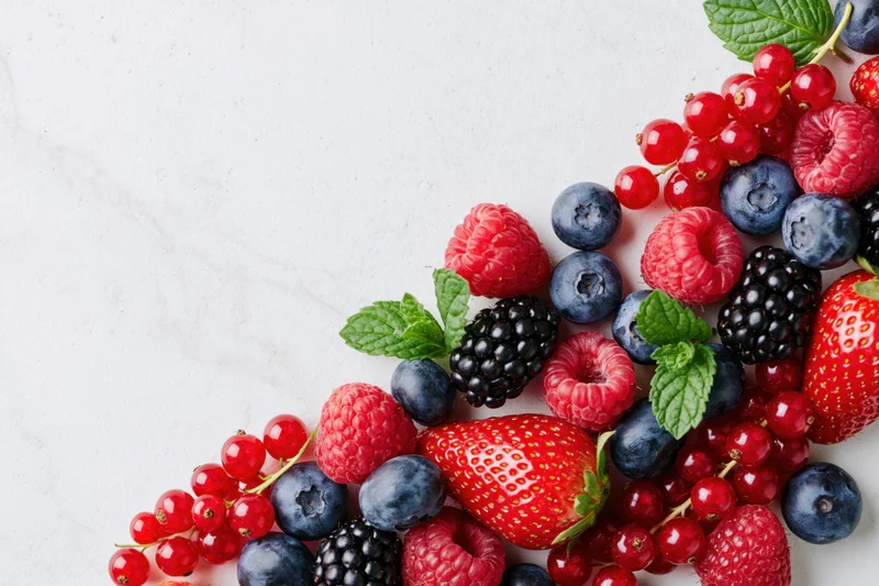 Assorted fresh berries and mint arranged along the right edge of a white marble surface