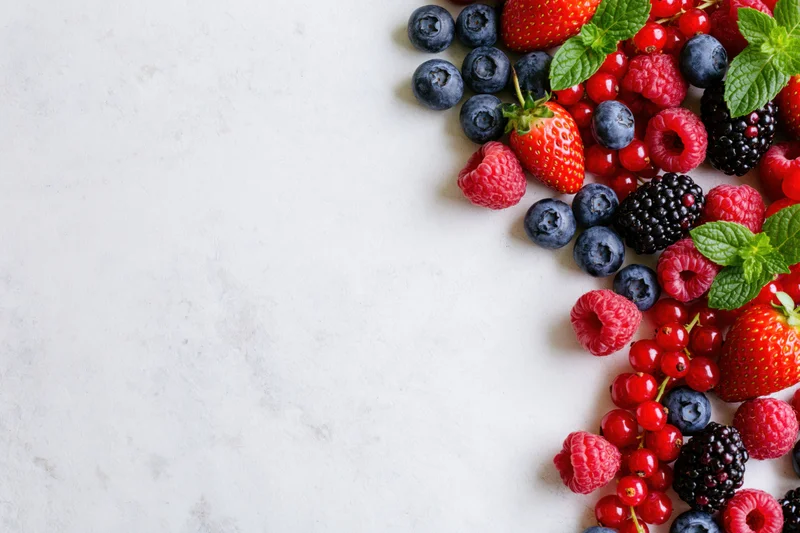 Assorted fresh berries arranged along the right edge of a white marble countertop