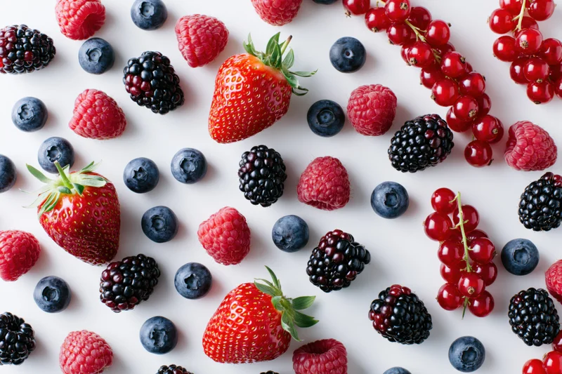 Assorted fresh berries scattered on a white surface in a flat lay arrangement
