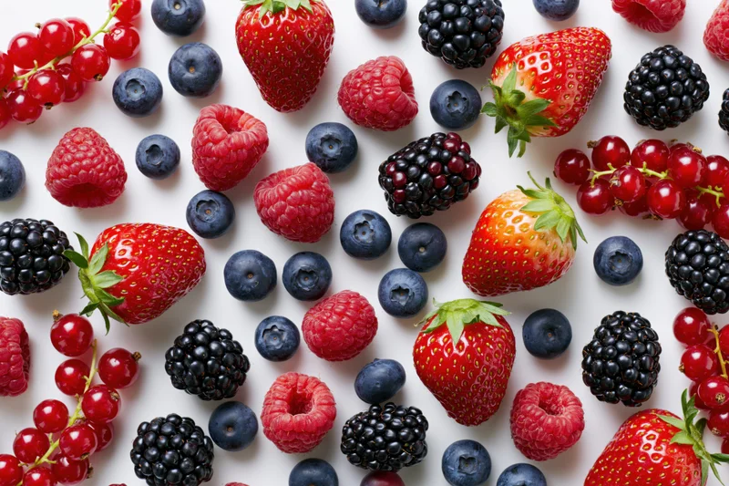 Assorted fresh berries scattered on a white surface in a flat lay arrangement