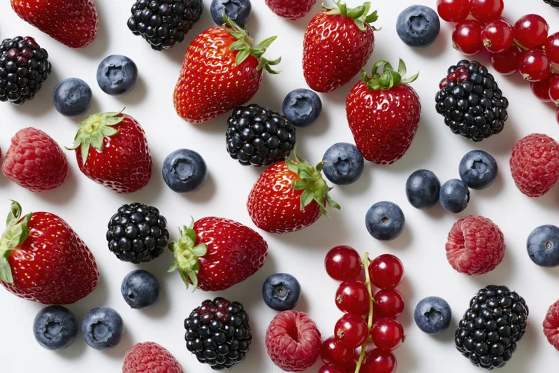 Assorted fresh berries scattered on a white surface in a flat lay overhead view