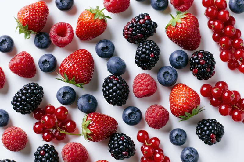 Assorted fresh berries scattered on a white surface in a flat lay arrangement