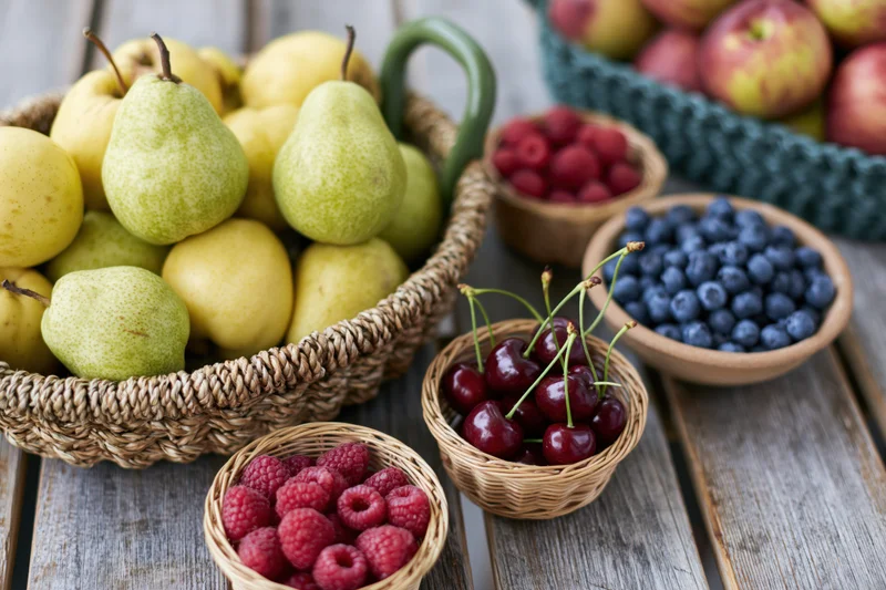 Assorted fresh fruit in woven baskets and small bowls on a wooden table