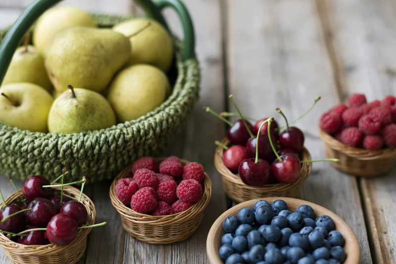 Assorted fresh fruit in woven baskets and small bowls on a wooden table