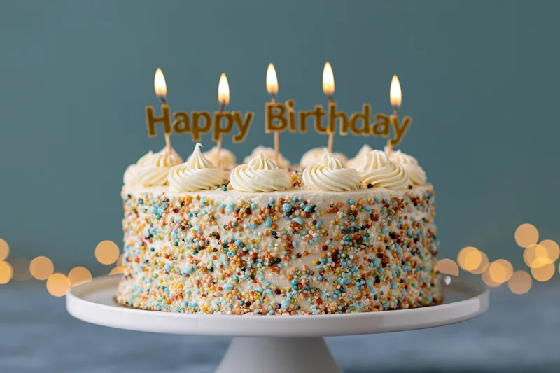 Birthday cake with lit candles and sprinkles on a white pedestal stand