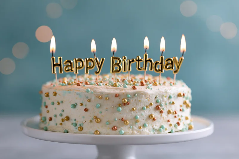 Birthday cake with lit candles and happy birthday topper on white pedestal stand
