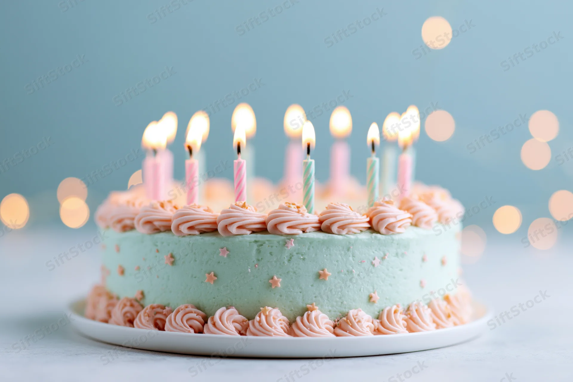Birthday cake with lit multicolored candles on a white plate against a blue background with bokeh lights