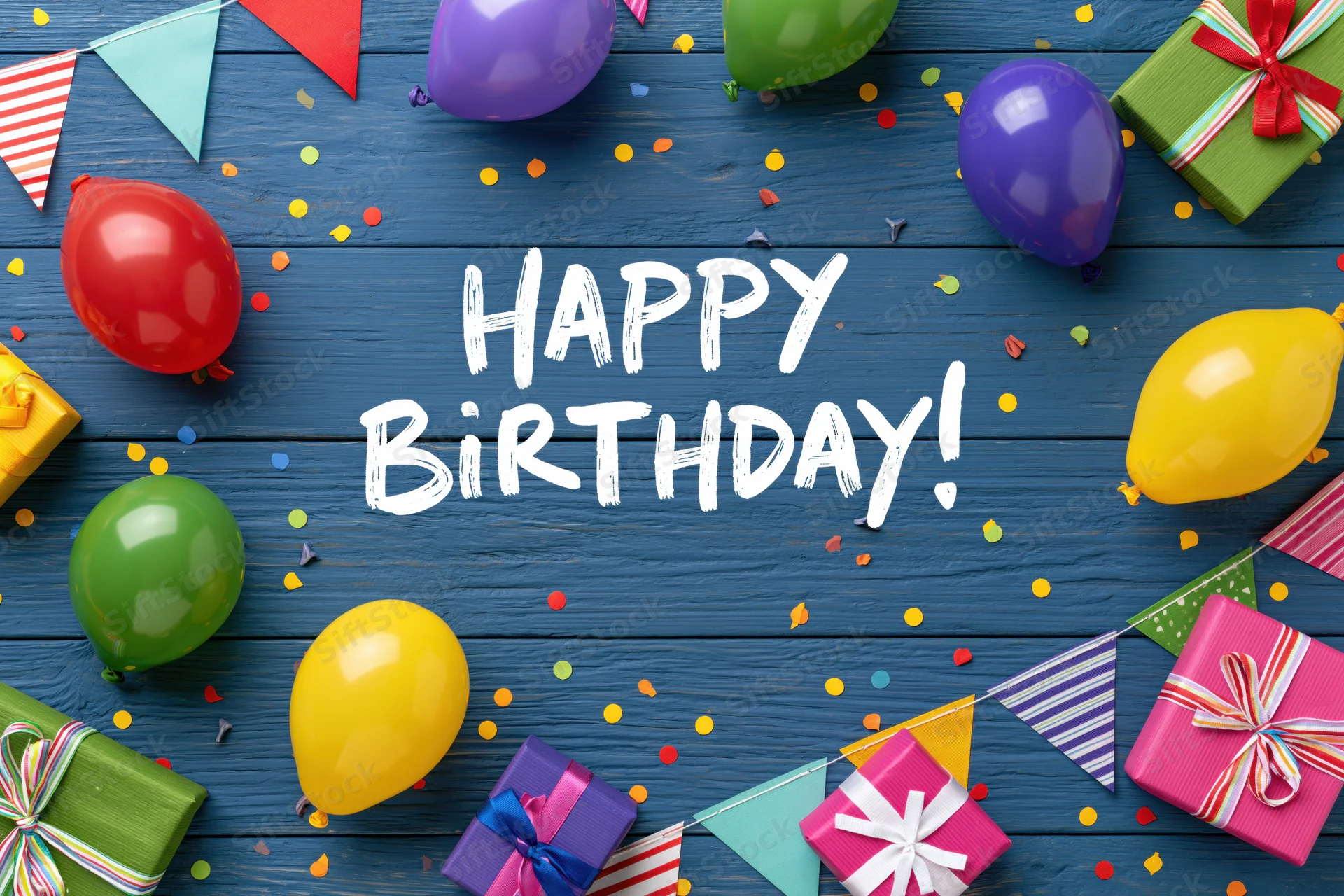 Colorful birthday party decorations with balloons and gifts arranged on blue wooden surface