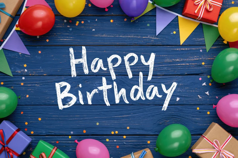 Colorful birthday party decorations and gifts arranged on blue wooden surface with happy birthday text in center