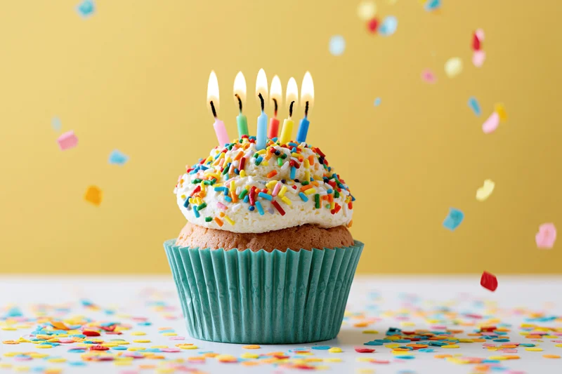 Birthday cupcake with lit multicolored candles and sprinkles on a yellow background