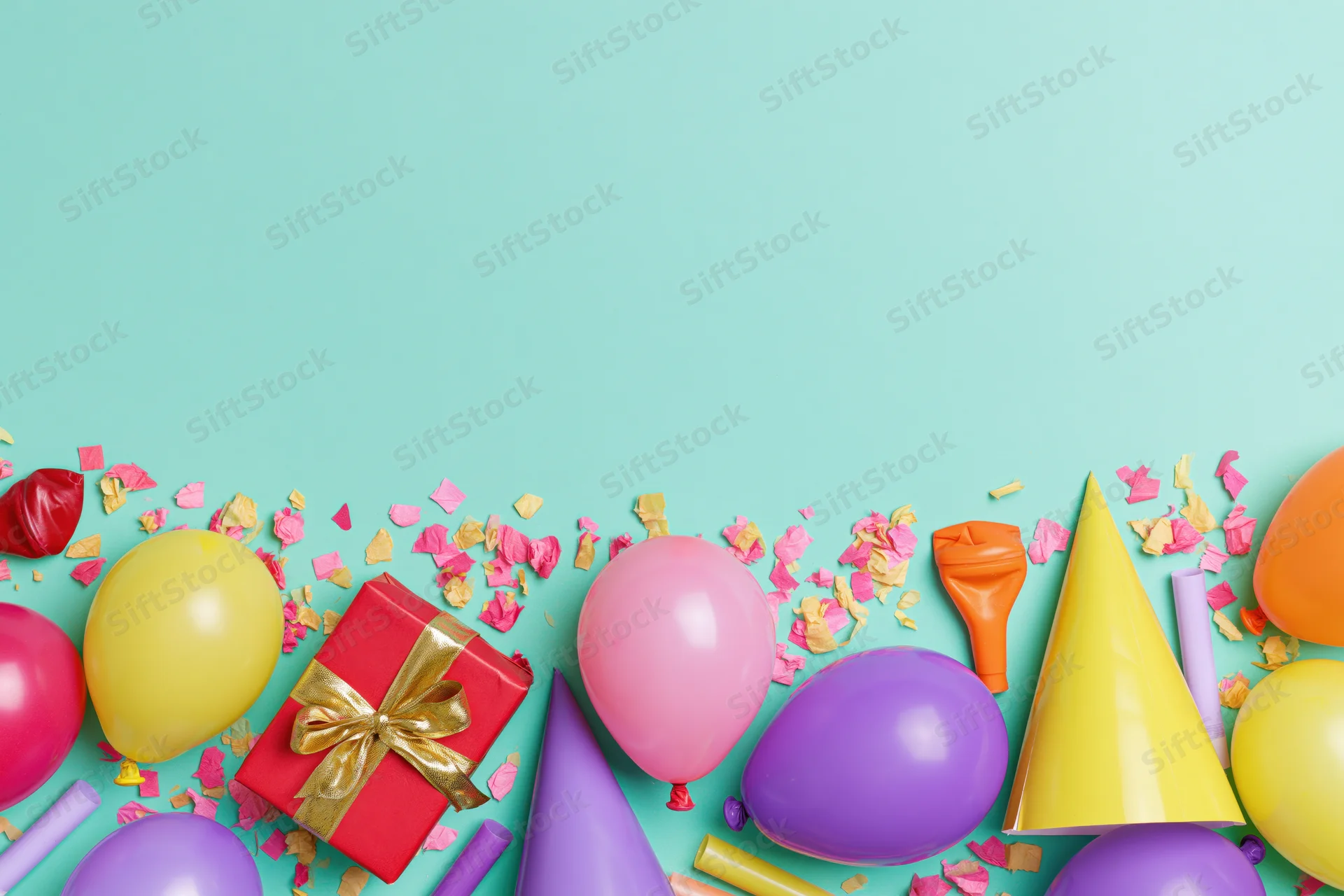 Birthday party supplies arranged along the bottom edge of a teal background with copyspace above