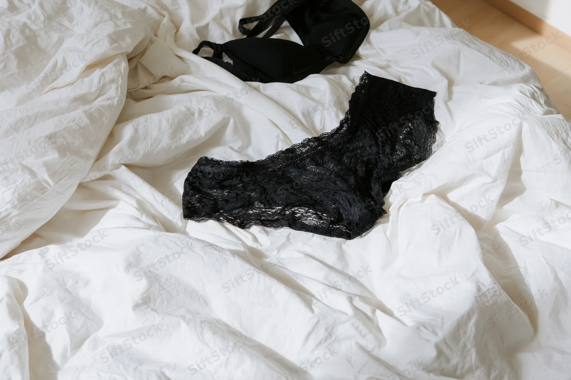 Black lace underwear and bra lying on rumpled white sheets in a bedroom