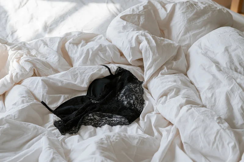 Black lace bra and underwear lying on rumpled white sheets in a bedroom