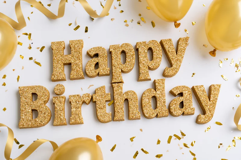 Gold glitter 3d happy birthday letters on white surface with balloons and confetti