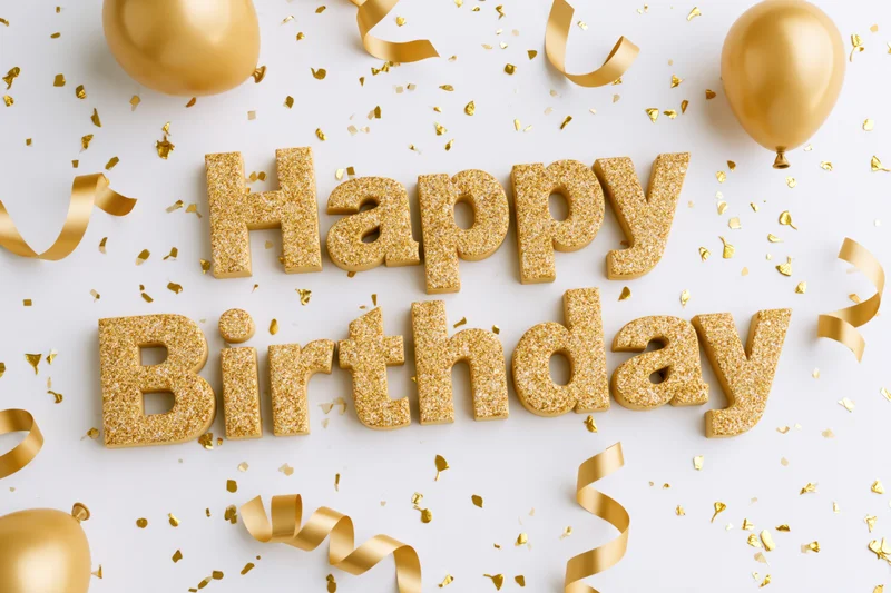 Gold glitter 3d happy birthday lettering on white surface with balloons and confetti