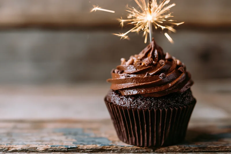 Chocolate cupcake with swirled frosting and sparkler on wooden surface