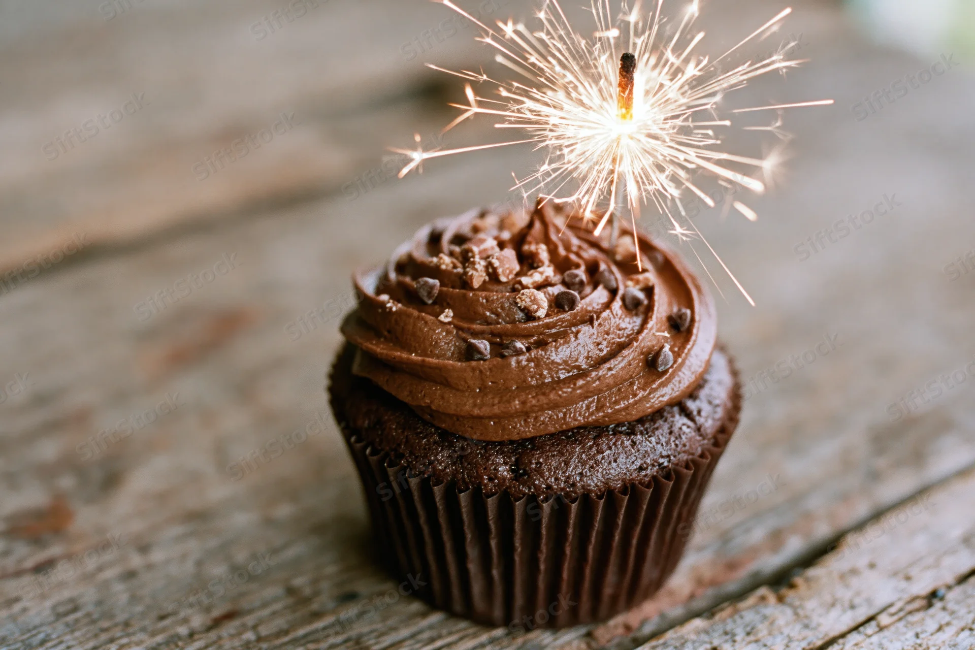 Chocolate cupcake with swirled frosting and sparkler on wooden table