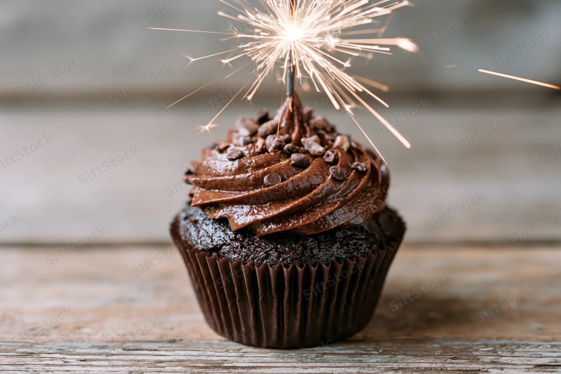 Chocolate cupcake with swirled frosting and sparkler on wooden table