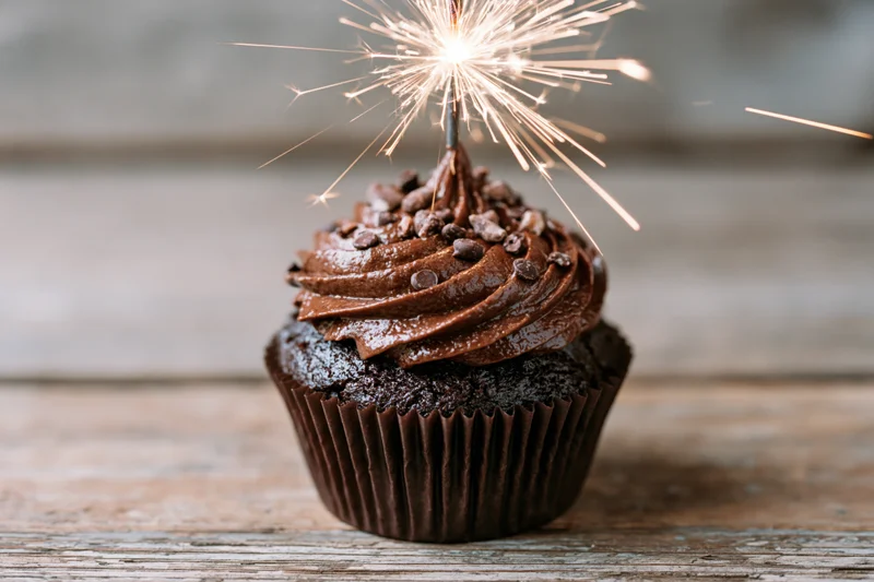 Chocolate cupcake with swirled frosting and sparkler on wooden table