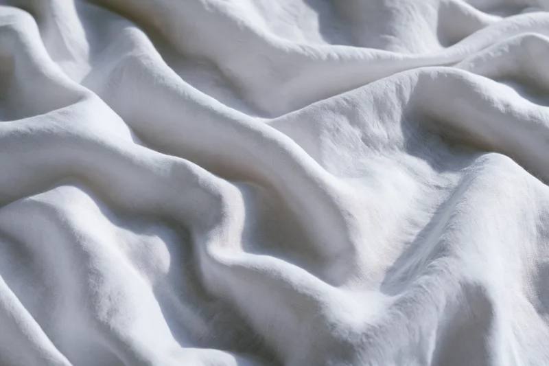 Crumpled white cotton bed sheet filling the frame in close-up flat lay