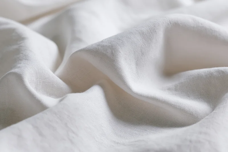 Close-up of crumpled white cotton fabric with soft folds and natural texture filling the frame